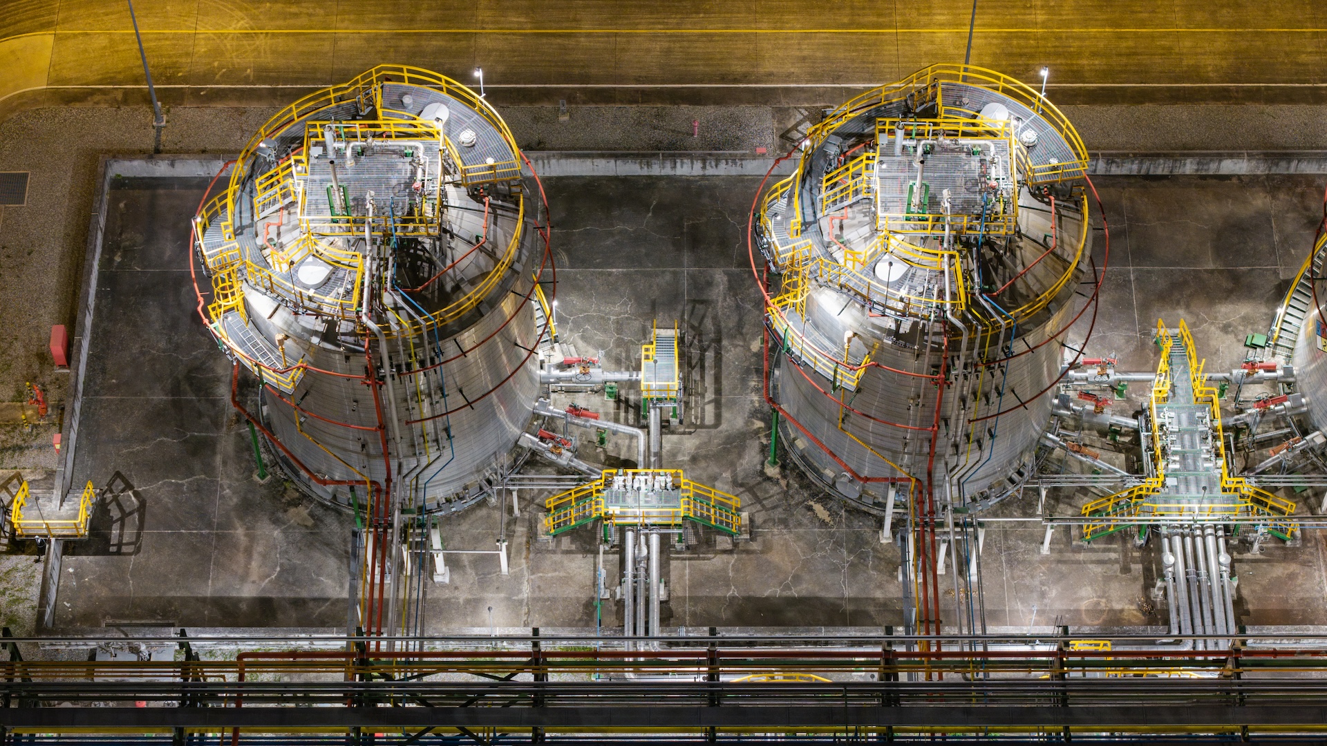 Detailed aerial view of an industrial refinery's intricate network of pipes, valves, and machinery illuminated at night, showcasing advanced operations.